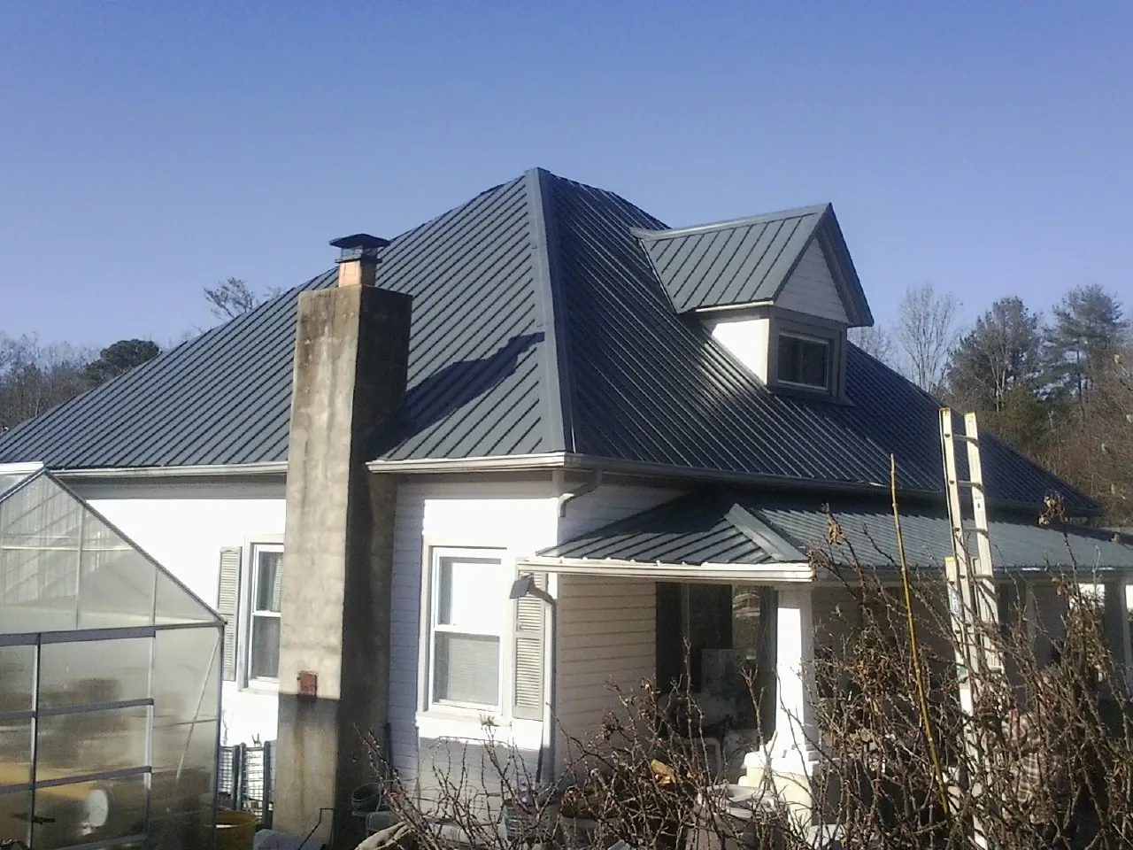 Dark blue standing seam metal roof on a white farmhouse with dormer — Slate & Tile Roof Repair by Roofing Brothers in Mad River