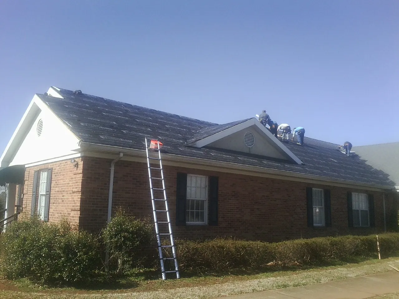 Crew tearing shingles off a brick ranch roof with a ladder set — Metal Roof Repair work by our crew in Mad River