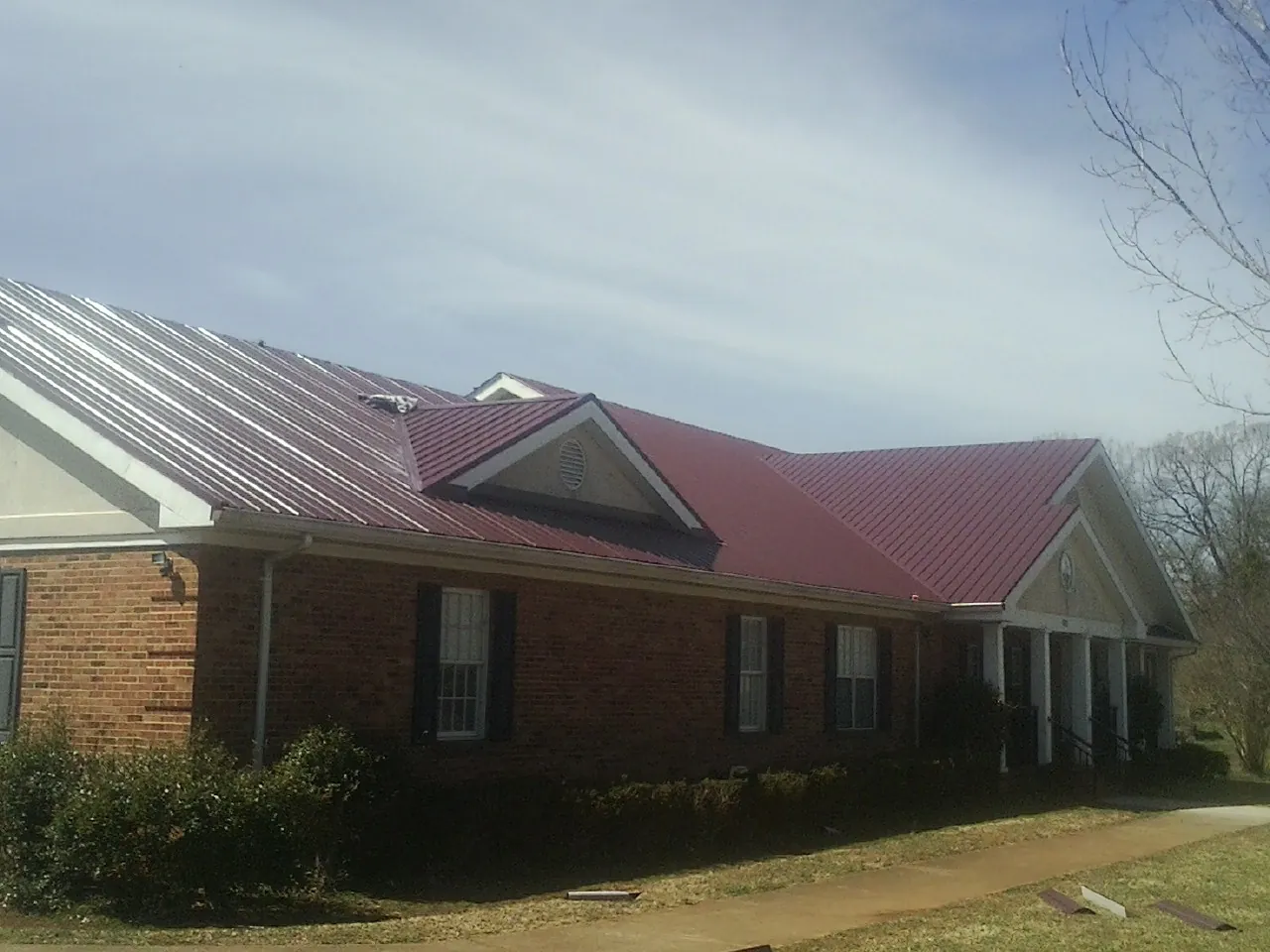 Red metal roof with gabled entries on a long brick building, from a Hail Damage Roof Repair job in Mad River