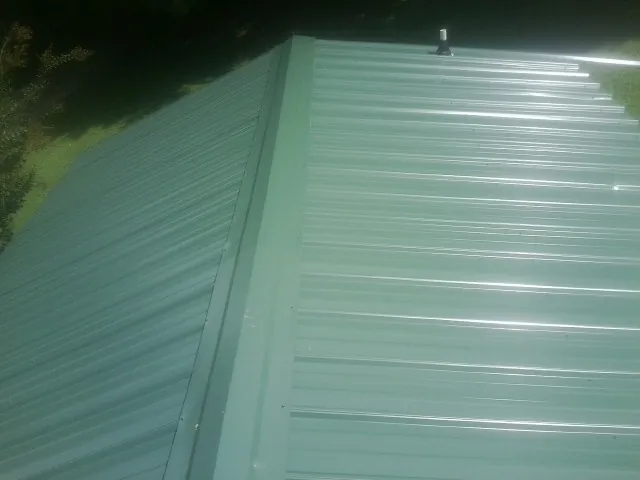 New green metal panels meeting at the ridge of a roof — Flat Roof Repair work by our crew in Mad River