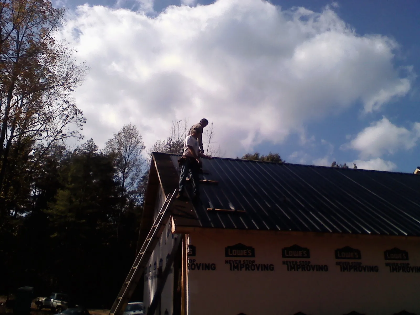 Roofer fastening dark metal panels high against a cloudy sky, from a Roof Inspection job in Mad River